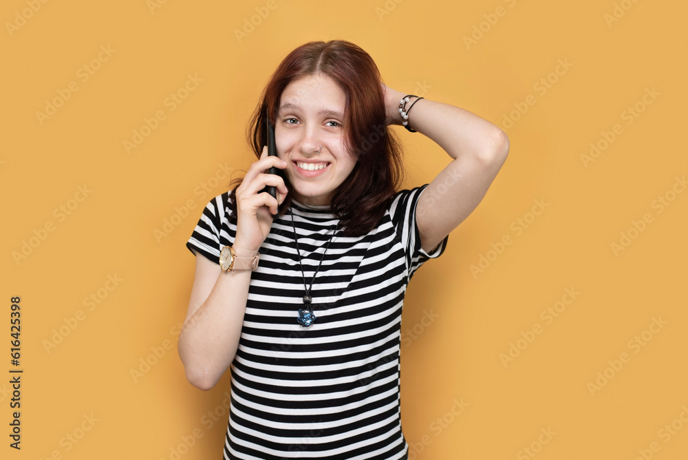 A teenage girl is talking on the phone with sarcasm on face, she listens to what her mother says and does the opposite. Emotions of mistrust, sarcasm in a girl's face on a yellow background A teenage girl is talking on the phone with sarcasm on face, she listens to what her mother says and does the opposite. Emotions of mistrust, sarcasm in a girl's face on a yellow background