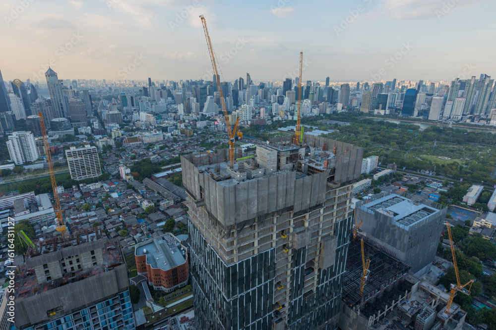 Fototapeta premium Aerial view of a large construction of a residential area with many multi-storey buildings under construction, a lot of tower cranes, workers, construction equipment at sunset 