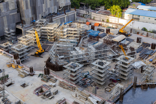 Aerial view of a large construction of a residential area with many multi-storey buildings under construction, a lot of tower cranes, workers, construction equipment at sunset
