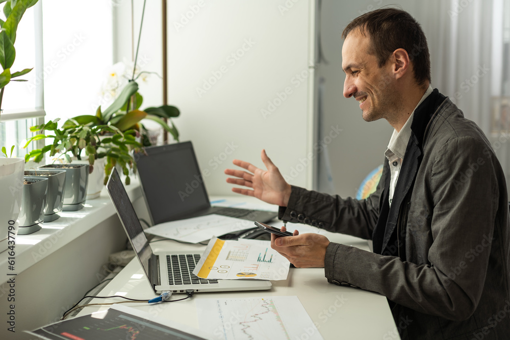 Happy joyful successful caucasian male stock investor, broker, sit at his work desk, looks at computer, rejoices in the growth of stock shares,