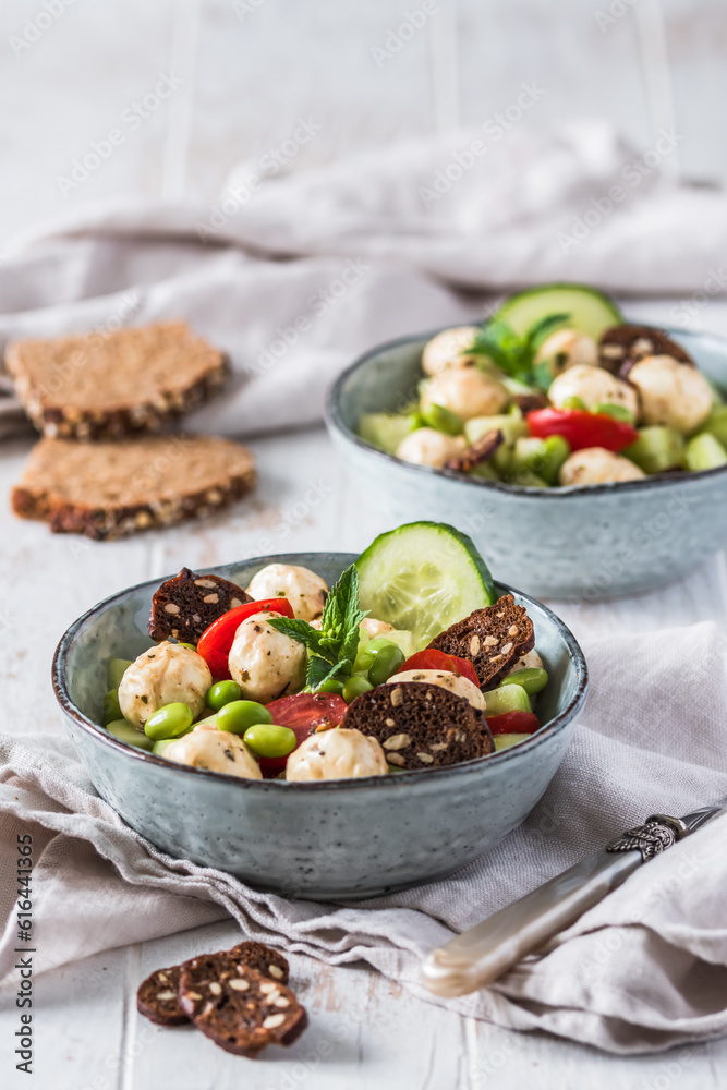 Summer salad with cucumber, mini tomatos, mini mozzarella and soybeans on white wooden background