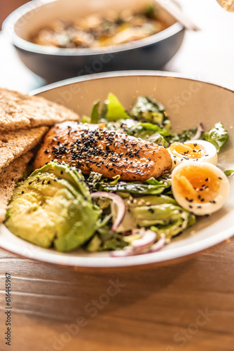 Fresh leaf salad served with avocado, eggs and grilled salmon on the top studded by sesame