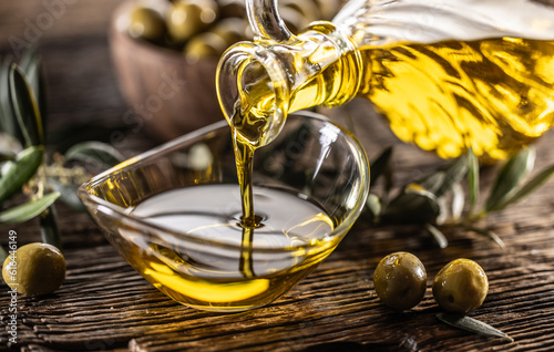 Obraz na plátne Pouring olive oil from carafe to the glass bowl and in background are olive bran