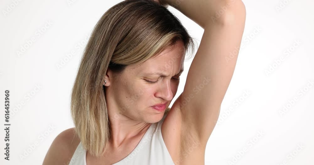 Worried woman with unhappy face checks smell of armpit. Bad underarm odor and bad smelling deodorant Worried woman with unhappy face checks smell of armpit. Bad underarm odor and bad smelling deodorant
