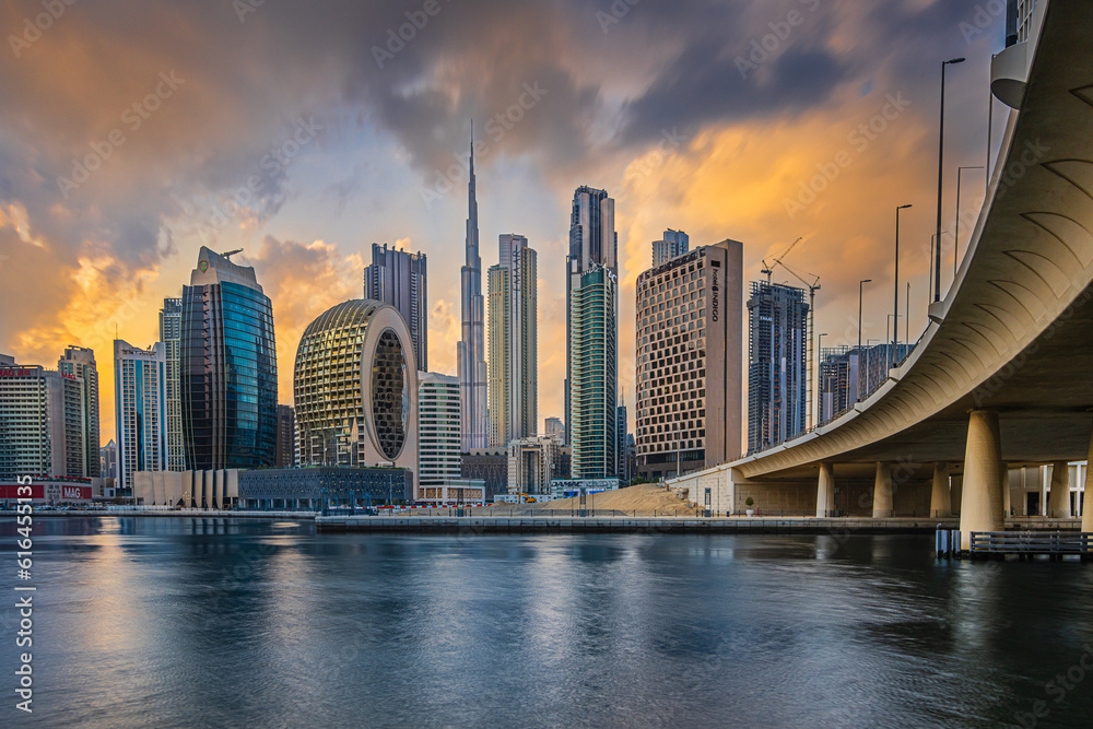 Evening mood in Dubai. Sunset with the city skyline in Emirates. Cloudy skies with skyscrapers overlooking Burj Khalifa. Glazed facade of skyscrapers. Bridge course road from the business center
