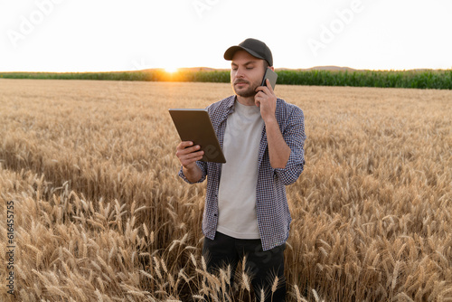 Fototapete Bearded farmer with mobile phone and digital tablet in agricultural field at sunset
