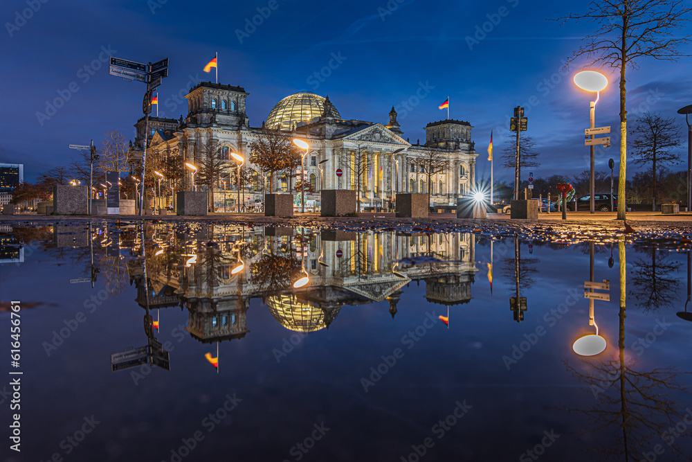 Reichstag in Berlin at the blue hour. Illuminated buildings and street lamps in the evening. Reflection of building on water surface. Evening mood in the winter of the capital of Germany