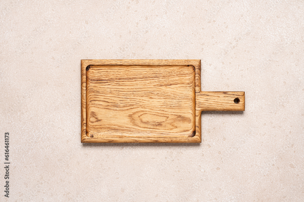 Fototapeta premium Wooden cutting board on beige light concrete background, top view