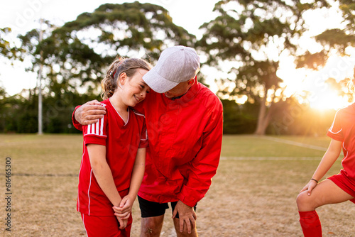 A male football coach with his arm around a player encouraging her