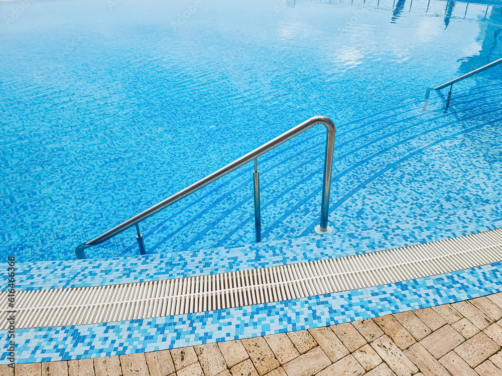 Beautiful pool with a Metal Handrails Descent and blue water at sunset. Swimming and summer rest concept.pool with a metal handrail. Safety for water sports