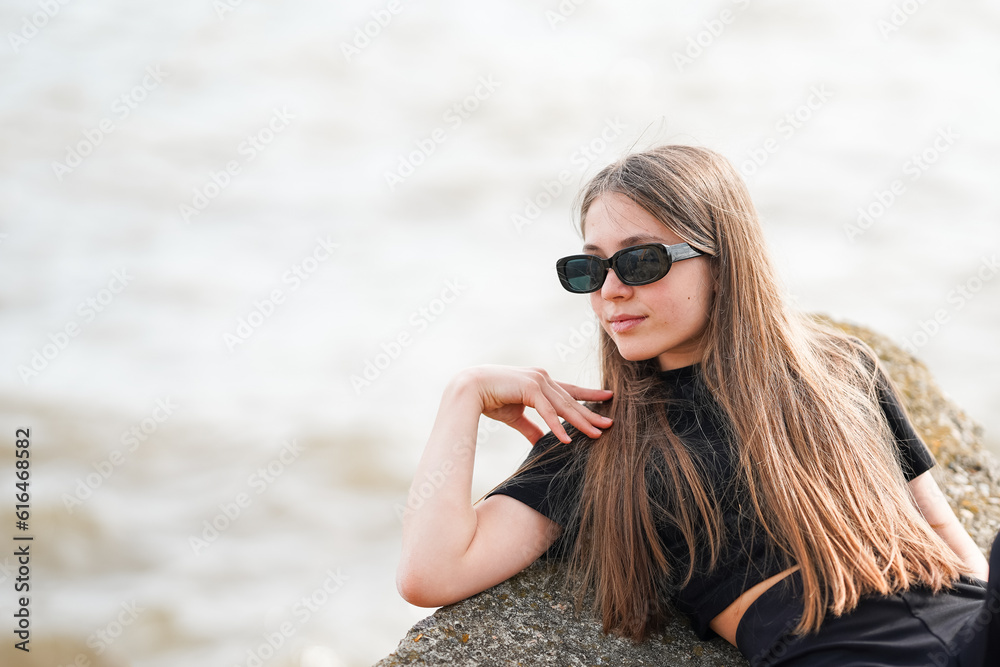 A beautiful young girl in sunglasses is lying on a rock on the seashore A beautiful young girl in sunglasses is lying on a rock on the seashore
