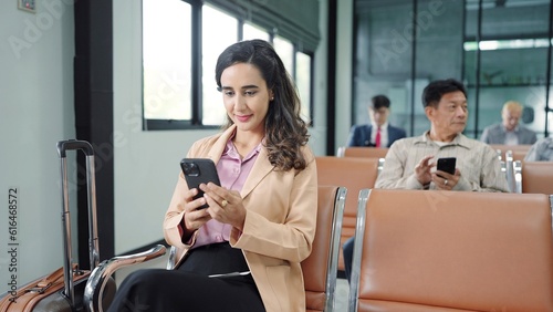 Young hispanic latin woman passenger using smartphone while sitting on chair in terminal departure gate waiting flight at international airport