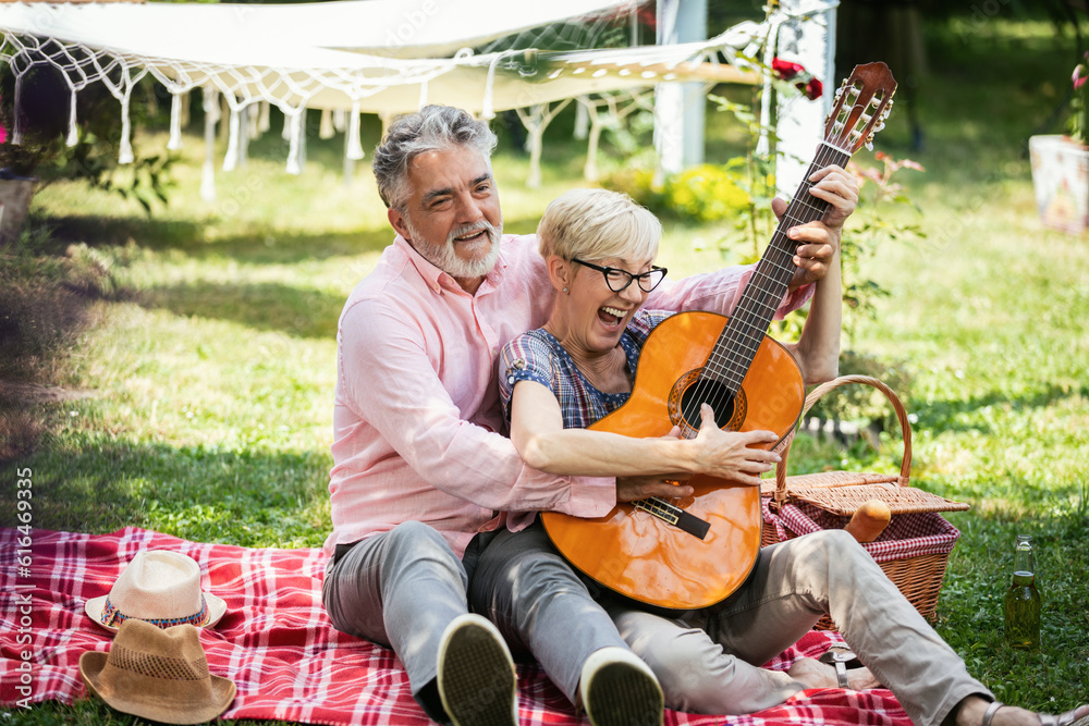 Elderly couple playing the guitar on grass. They are Having fun and celebrating on a picnic