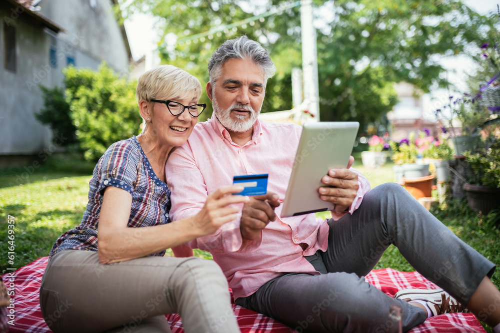 Elderly couple buying online with their card.Sitting in the backyard while having a picnic. Elderly couple buying online with their card.Sitting in the backyard while having a picnic.