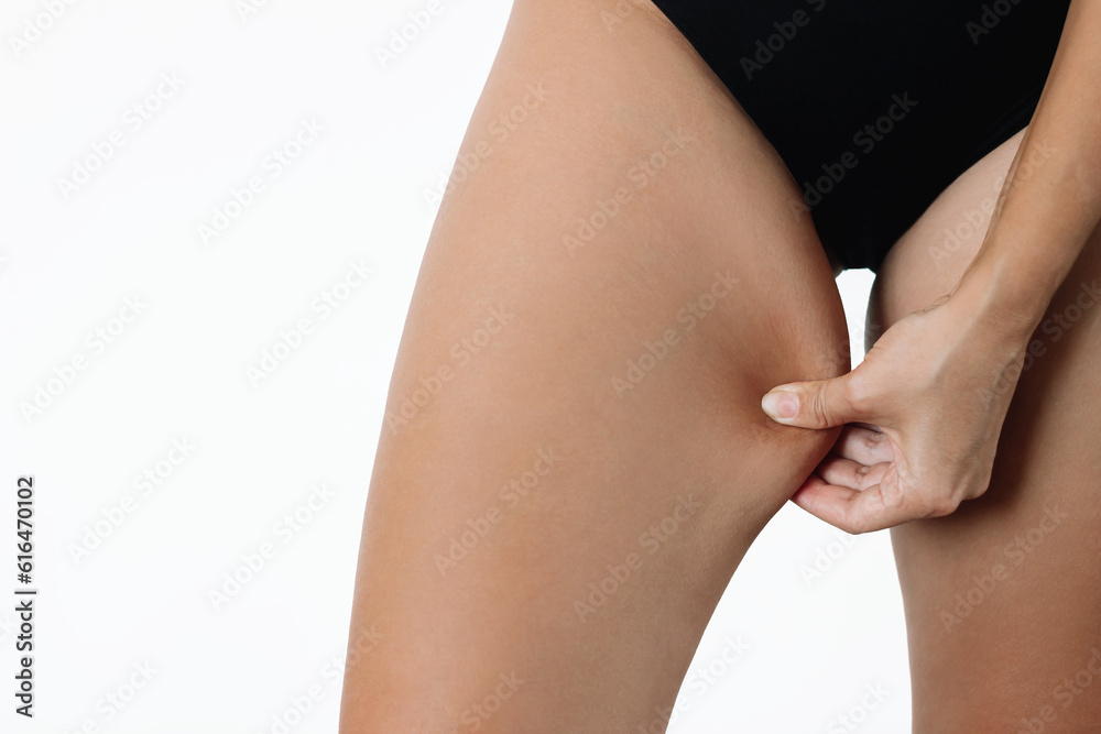 Cropped shot of a young woman grabbing skin on her inner thigh with excess fat isolated on a white background. Pinching the loose and saggy muscles. Problem area of hips, overweight. Chafing the skin - obrazy, fototapety, plakaty 