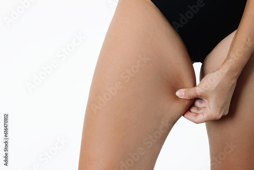 Cropped shot of a young woman grabbing skin on her inner thigh with excess fat isolated on a white background. Pinching the loose and saggy muscles. Problem area of hips, overweight. Chafing the skin photo