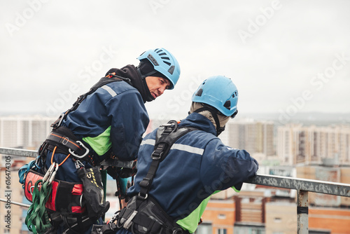 Rear view Industrial mountaineer laborers in uniform posing on roof residential house, looking around. From behind of two access workers, high rise work. Concept of industry urban work. Copy ad space