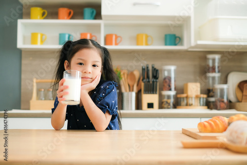 Cute little girl holding a glass of milk in the kitchen to drink milk for breakfast,Food and health nutrition beverage concept.