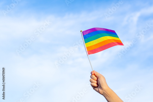 rainbow gay flag in hand waving against clear blue sky space, LGBTQ people doing activities celebrating equality sexual freedom, diversity of genders, love and protecting the rights of individual