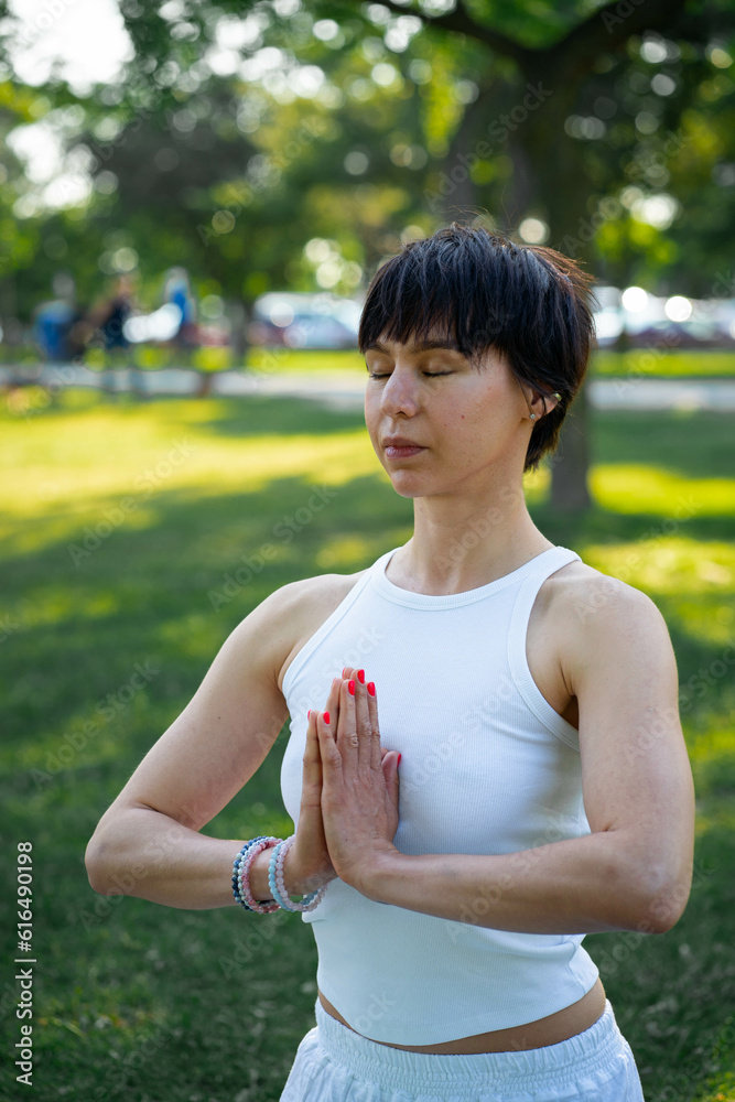 Motion past lady yoga practitioner in new white sportwear sitting in lotus position with namaste on mat in lin the Park Motion past lady yoga practitioner in new white sportwear sitting in lotus position with namaste on mat in lin the Park