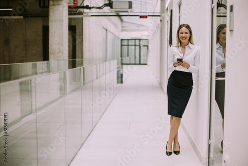Young business woman using mobile phone in the office hallway