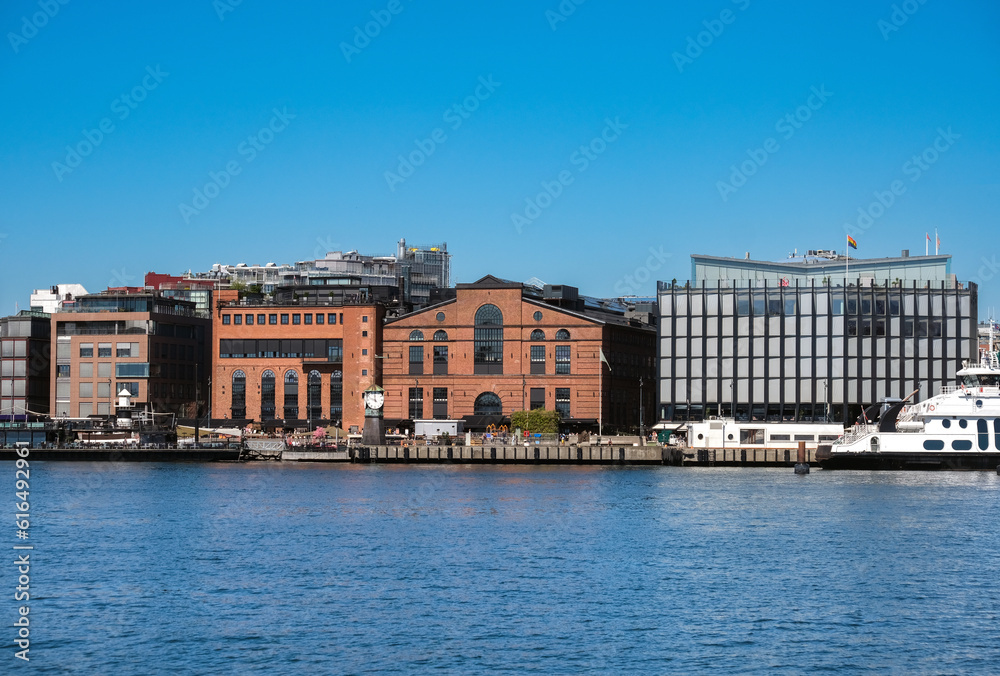 Sommerlicher Blick auf Norwegens Hauptstadt Oslo: Teilansicht eines zentralen Stadtviertels vom Hafen aus mit Restaurants und Cafés und einer Fähre