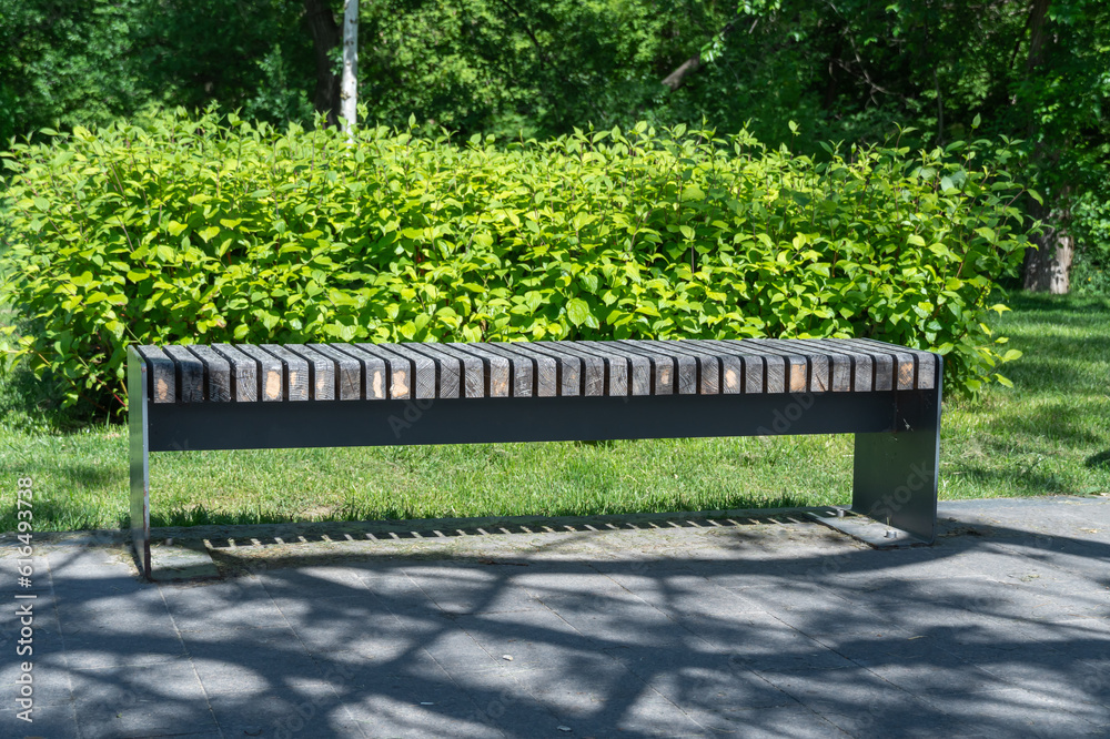 Comfortable in metal and wooden material bench in city park. Design of black and brown stationary seat for leisure. Geometry on nature and place to rest. Exterior empty park bench. Furniture in garden