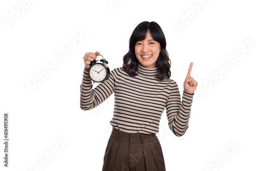 Smiling cheerful attractive young asian woman wearing sweater shirt holding alarm clock, point finger above and looking camera isolated on white background, studio portrait