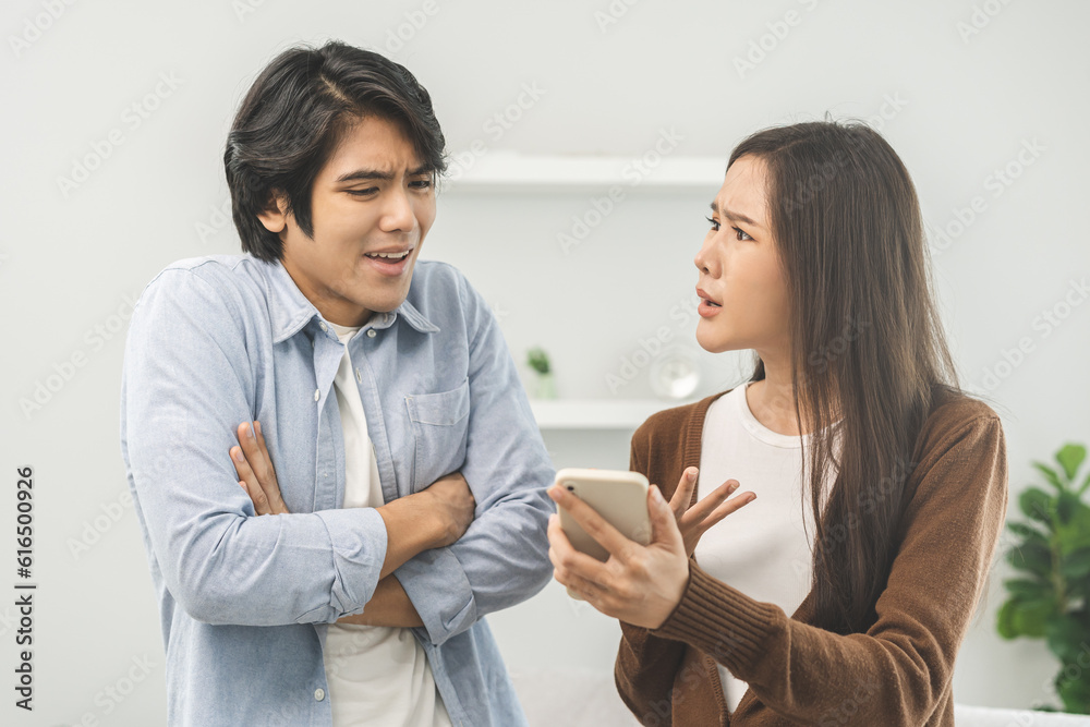 Infidelity, suspicion asian young couple love fight relationship, wife holding cellphone, smartphone cheating on phone, scolding husband about mistrust, distrust and jealousy when sitting at home. Infidelity, suspicion asian young couple love fight relationship, wife holding cellphone, smartphone cheating on phone, scolding husband about mistrust, distrust and jealousy when sitting at home.