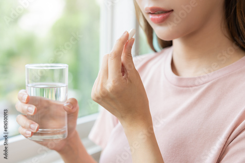 Sick, asian young woman, girl hand holding pill capsule, painkiller medicine from stomach pain, head ache, pain for treatment, take drug or vitamin and glass of water at home, pharmacy and health care