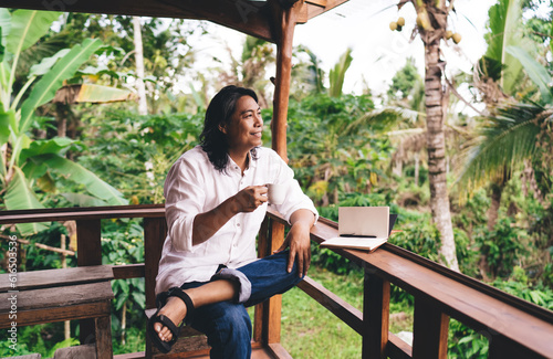 Smiling Indonesian entrepreneur drinking coffee while sitting on terrace