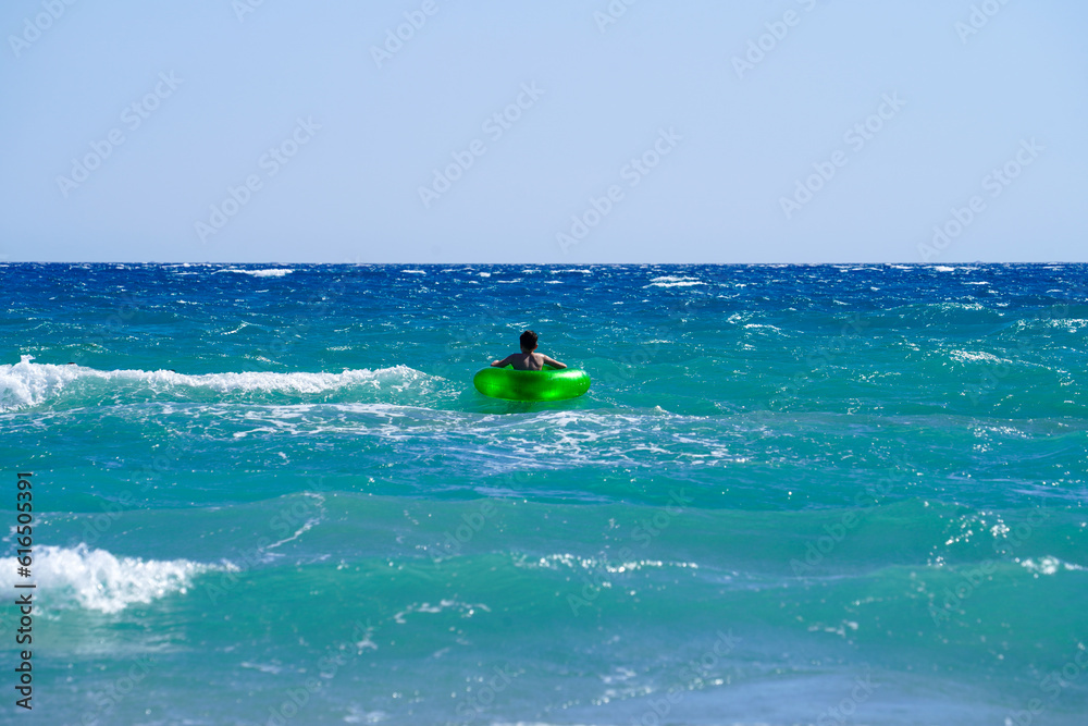 Child swims far far away with swimming ring in the middle of wavy mediterranean sea Child swims far far away with swimming ring in the middle of wavy mediterranean sea