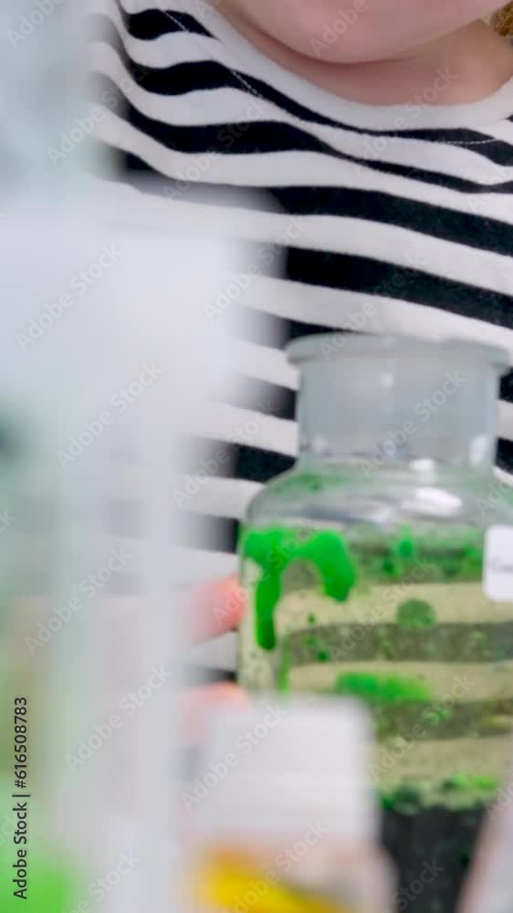 Close up of pipette water drop intro glass test tube in laboratory a little girl plays in a chemical laboratory with green paint in a striped t-shirt, only her hands and a test tube are visible Close up of pipette water drop intro glass test tube in laboratory a little girl plays in a chemical laboratory with green paint in a striped t-shirt, only her hands and a test tube are visible