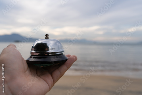service bell in hand, beach and ocean in background