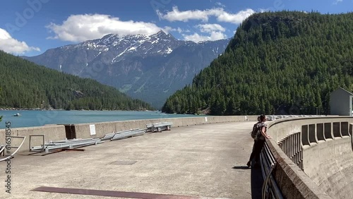 Panning shot of a woman taking in the view from Ross Dam towards the turquoise lake and mountains on a sunny, summer day - North Cascades National Park, Washington, USA photo