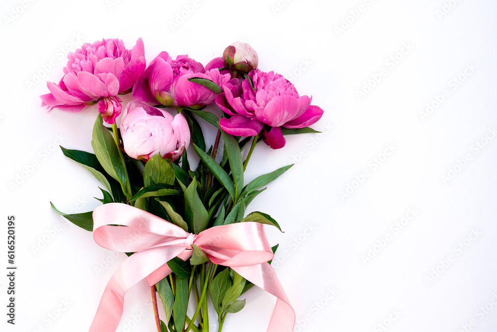 Bouquet of pink Peonies tied with a pink bow. Spring flowers on the white background. Flower arrangement of pink peonies and place for text. Flower bouquet, lat lay. Pink flowers with a ribbon.