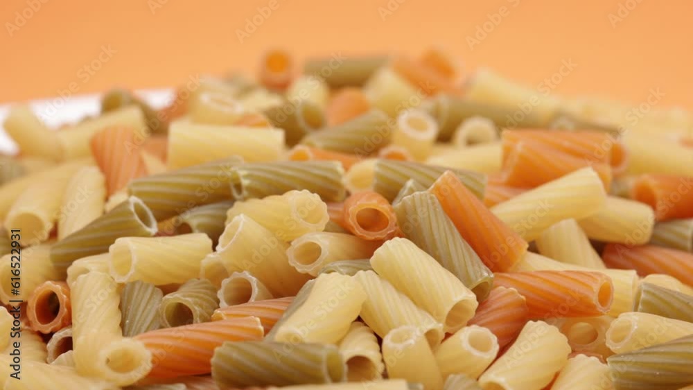 Raw Italian Multicolored Pasta In A White Plate On Orange Background. Elicoidali. Rotating. 4k, 60 FPS, ProRes. Raw Italian Multicolored Pasta In A White Plate On Orange Background. Elicoidali. Rotating. 4k, 60 FPS, ProRes.