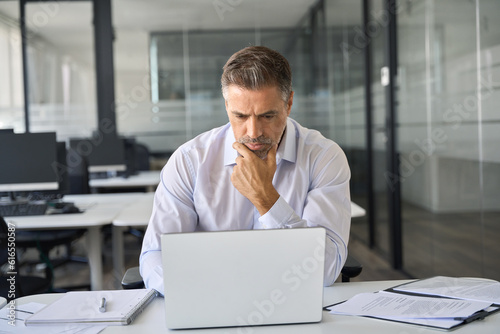 Valokuva Serious busy mature professional business man company ceo executive manager investor looking at laptop pc computer sitting in office thinking of corporate management plan and financial strategy risks