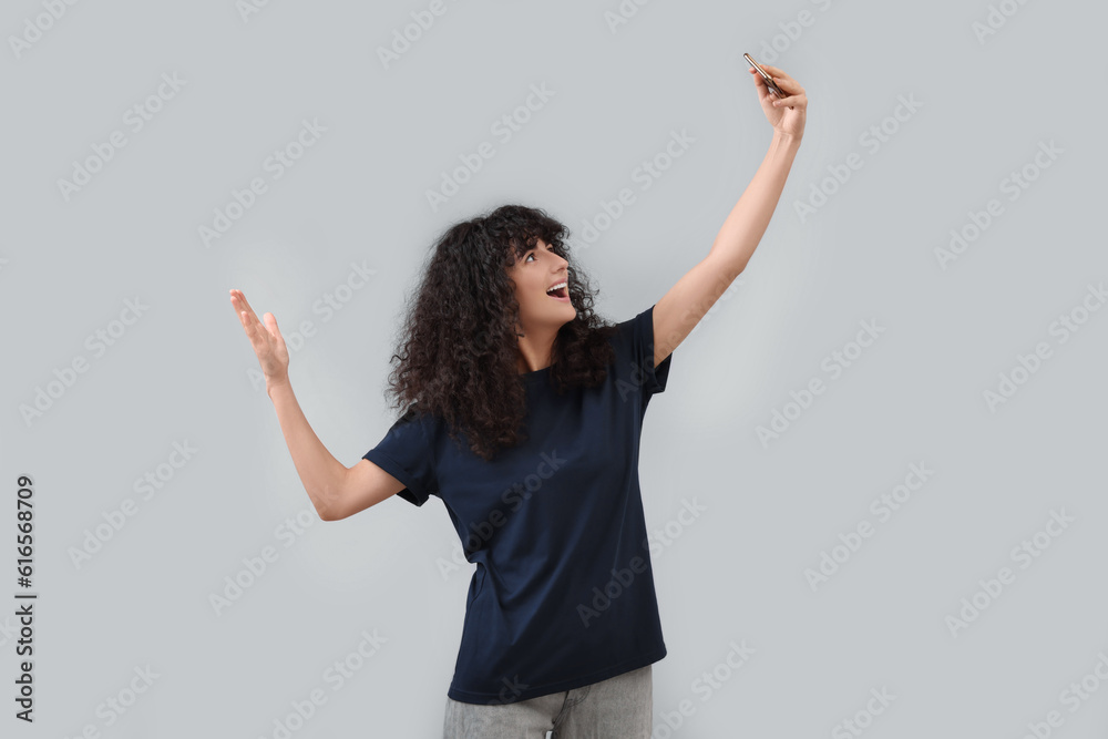 Beautiful young woman taking selfie on light grey background Beautiful young woman taking selfie on light grey background