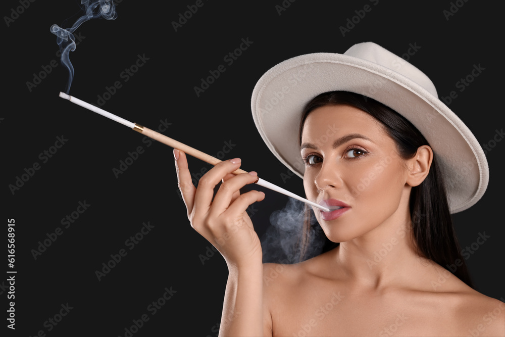 Fototapeta premium Woman using long cigarette holder for smoking on black background