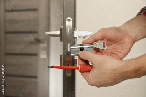Handyman changing core of door lock indoors, closeup. Space for text photo