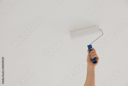 Worker painting ceiling with roller indoors, closeup. Space for text