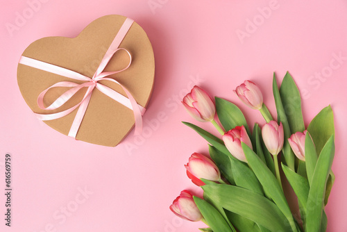 Heart shaped gift box with bow and beautiful tulips on pale pink background, flat lay