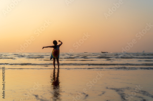 back asian child or kid girl standing on summer sand beach and sea to happy raising hands with golden warm sunlight on sunset twilight or morning sunrise for family vacation travel on holiday relax