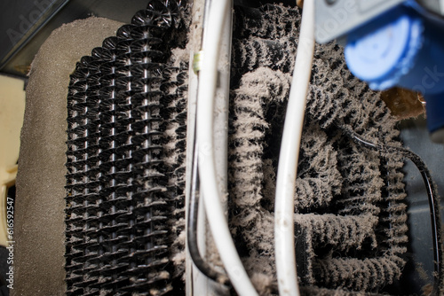 Fridge condenser coils covered in dust and pet hair. Maintenance concept Refrigerator and repair of kitchen appliances. 