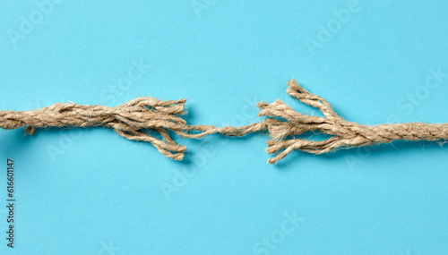 Tension, separation, danger or risk concepts. Frayed rope is about to brake on blue background with copy space. photo