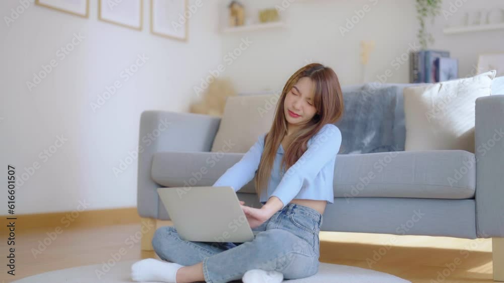 Office syndrome concept. Asian young woman working on laptop while seated on floor next to couch at home, feeling pain in neck and shoulder after working on computer laptop for a long time Office syndrome concept. Asian young woman working on laptop while seated on floor next to couch at home, feeling pain in neck and shoulder after working on computer laptop for a long time
