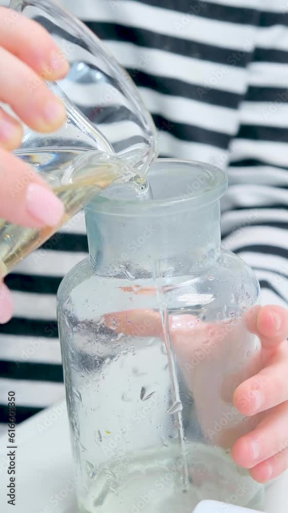 the hands of a child and a woman in small stream pour sunflower oil mixed with water into a glass bottle from a glass flask, a special liquid for chemical experiments children's laboratory the hands of a child and a woman in small stream pour sunflower oil mixed with water into a glass bottle from a glass flask, a special liquid for chemical experiments children's laboratory