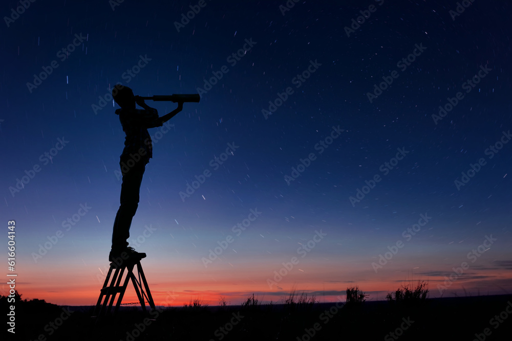 The child looks at the stars through a telescope. A teenager boy looks at the night sky through a spyglass against the backdrop of a sunset while in the field.