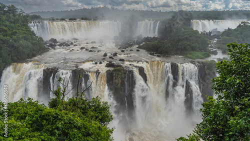 Streams of the waterfall cascades down from the ledges. Stones in the riverbed. Fog  spray in the air. Lush tropical vegetation. Iguazu Falls. Brazil.